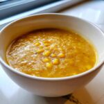 A close-up view of thick, creamy corn soup garnished with whole kernels in a simple white bowl.