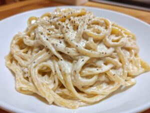 Close-up of spaghetti noodles coated in creamy cottage cheese alfredo sauce and topped with black pepper.