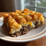 A hearty slice of tater tot casserole showing crispy tots, melted cheese, and ground beef filling.