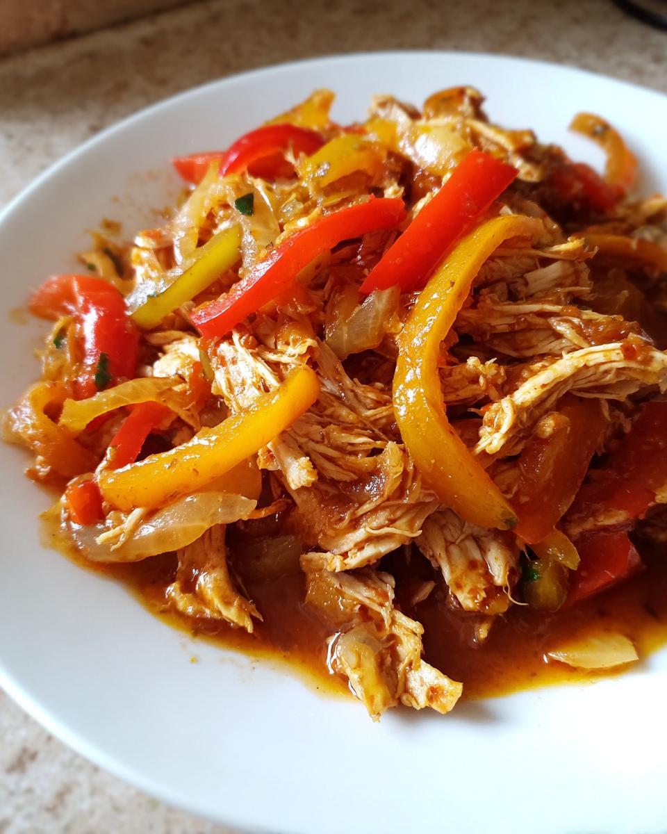 Close-up of shredded chicken mixed with colorful bell peppers and onions, ready for crockpot chicken fajitas.