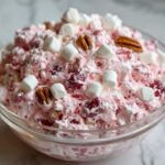 Close-up of a bowl of fluffy pink cranberry salad topped with mini marshmallows and pecans.