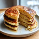 A tall stack of fluffy discard pancakes, with a slice removed to show the airy interior, drizzled with syrup.
