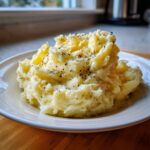 A generous serving of fluffy mashed potatoes recipe, topped with freshly cracked black pepper, on a white plate.