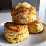 A stack of three fluffy sweet potato biscuits topped with melting honey butter on a white plate.