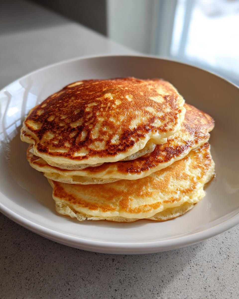 A stack of three fluffy greek yogurt pancakes with golden-brown tops served in a light bowl.