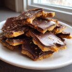 A pile of broken pieces of graham cracker toffee with a thick chocolate topping served on a white plate.