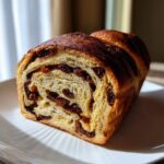 A close-up, appetizing view of a freshly baked loaf of raisin bread showing the swirl of dark raisins inside the golden crumb.