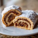 Two halves of Italian nut roll cookies, showing the rich, swirled nut filling and dusted heavily with powdered sugar.