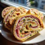 Close-up of several slices of savory Italian pinwheels made with rolled egg, ham, and cream cheese, garnished with herbs.