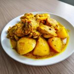 Close-up of rich Jamaican curry chicken pieces served with large chunks of yellow potato in a vibrant curry sauce.