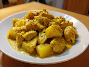 Close-up of vibrant yellow Jamaican curry chicken and chunks of potato served on a white plate.
