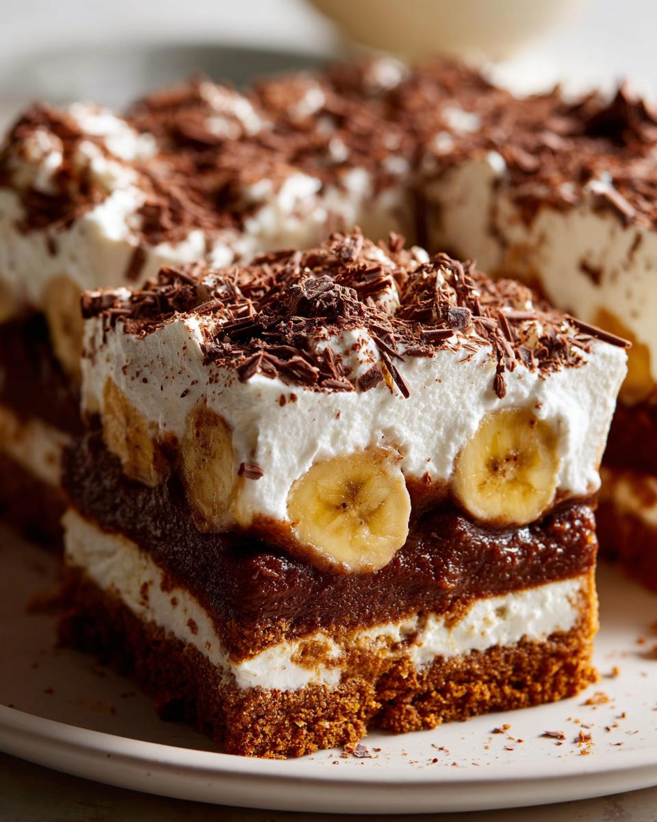 Close-up of a rich slice of banoffee pie showing layers of cake, cream, bananas, and chocolate shavings.