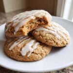 A stack of soft maple brown sugar cookies drizzled with white icing, one cookie is broken open.