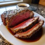 Close-up of a perfectly cooked medium-rare rib roast, sliced and resting in its juices.