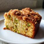 Close-up of a moist slice of pistachio coffee cake featuring bright green pistachio pieces and a thick brown sugar crumb topping.