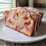 Close-up of a moist slice of strawberry bread studded with fresh strawberries and topped with a pink glaze.