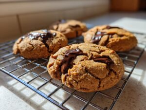 Close-up of gooey peanut butter chocolate chip cookies cooling on a wire rack in natural light.