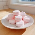 A stack of fluffy, light pink cream cheese mints dusted with powdered sugar on a white plate.