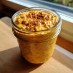A close-up view of creamy pumpkin pie overnight oats topped with cinnamon in a glass jar.