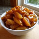 Close-up of a white bowl overflowing with glossy, spiced apple pie filling, ready for baking.
