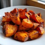 Close-up of perfectly roasted, caramelized sweet potatoes cubes served in a white bowl.