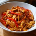 Close-up of shredded chicken mixed with vibrant red bell pepper strips, ready for crockpot chicken fajitas.