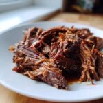 Close-up of tender, shredded Mississippi pot roast piled high on a white plate.