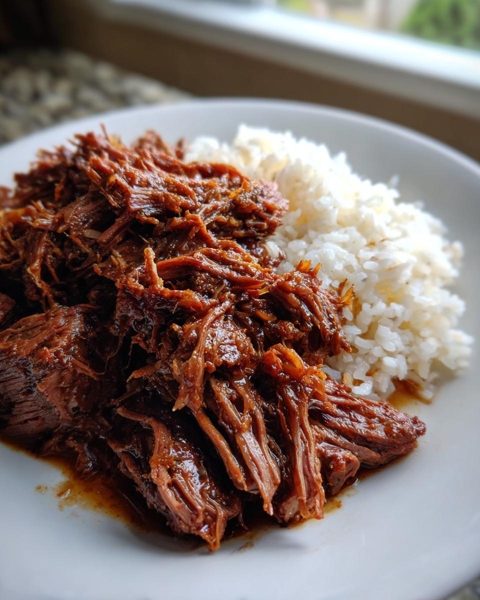 A close-up of tender, shredded mississippi pot roast coated in rich gravy next to a serving of fluffy white rice.