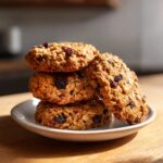 A close-up stack of four soft oatmeal raisin cookies resting on a small white plate.
