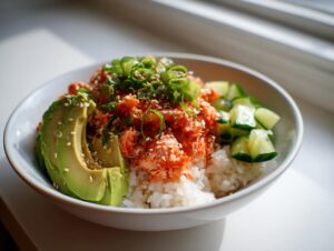 A close-up of a spicy crab sushi bowl featuring rice topped with spicy crab mix, sliced avocado, cucumber, and sesame seeds.