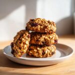 A stack of four hearty, oatmeal-based breakfast cookies studded with dried cranberries, sitting on a small plate.