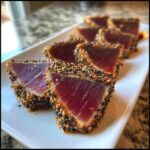 Close-up of perfectly seared tuna tataki slices coated in a black and white sesame seed crust, served on a white platter.