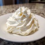 A perfect, fluffy swirl of white vanilla buttercream frosting piped onto a small white plate.
