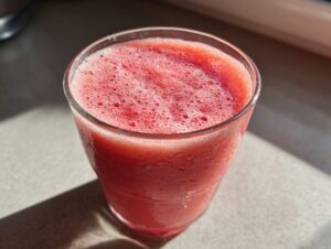 Close-up of a vibrant, frosty watermelon smoothie with a foamy top in a clear glass.