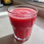 A close-up of a vibrant, icy watermelon smoothie in a sweating glass on a bright windowsill.