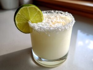 Close-up of a creamy white Christmas margarita garnished with a lime wheel and shredded coconut rim.