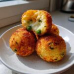 A stack of golden brown air fryer arancini balls, one cut open showing melted cheese and peas inside.