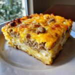 A hearty slice of baked breakfast casserole featuring layers of eggs, sausage, and melted cheddar cheese.
