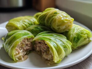 A plate of steamed cabbage dumplings, one cut open to show the savory ground meat and rice filling.