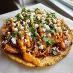 A single, crispy chicken tostadas piled high with shredded chicken, drizzled with orange sauce, crumbled white cheese, and fresh cilantro.