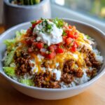Close-up of a delicious taco rice bowl layered with seasoned ground beef, rice, lettuce, cheese, salsa, and sour cream.