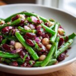 Close-up of a vibrant three bean salad featuring bright green beans, dark red kidney beans, chickpeas, and red onion.