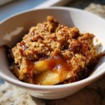 Close-up of a serving of apple crisp with salted caramel drizzled over the oat topping.