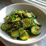 Close-up of a bowl of refreshing Asian cucumber salad, tossed in dark dressing and topped with toasted sesame seeds.