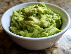 A close-up of chunky, bright green authentic guacamole served in a small white bowl.