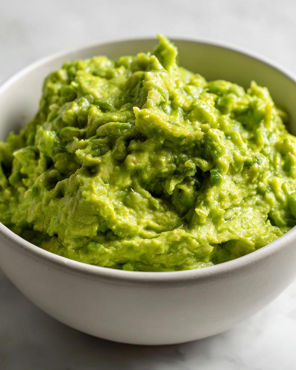 Close-up of vibrant green, chunky Authentic guacamole served in a simple white bowl.