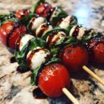 Close-up of several delicious caprese skewers featuring cherry tomatoes, mozzarella balls, basil, and drizzled balsamic glaze.