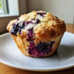 A close-up of a perfectly baked blueberry cottage cheese muffin with a golden top sprinkled with sugar.