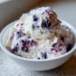 Close-up of scoops of creamy white blueberry fluff salad mixed with dark purple blueberries in a white bowl.