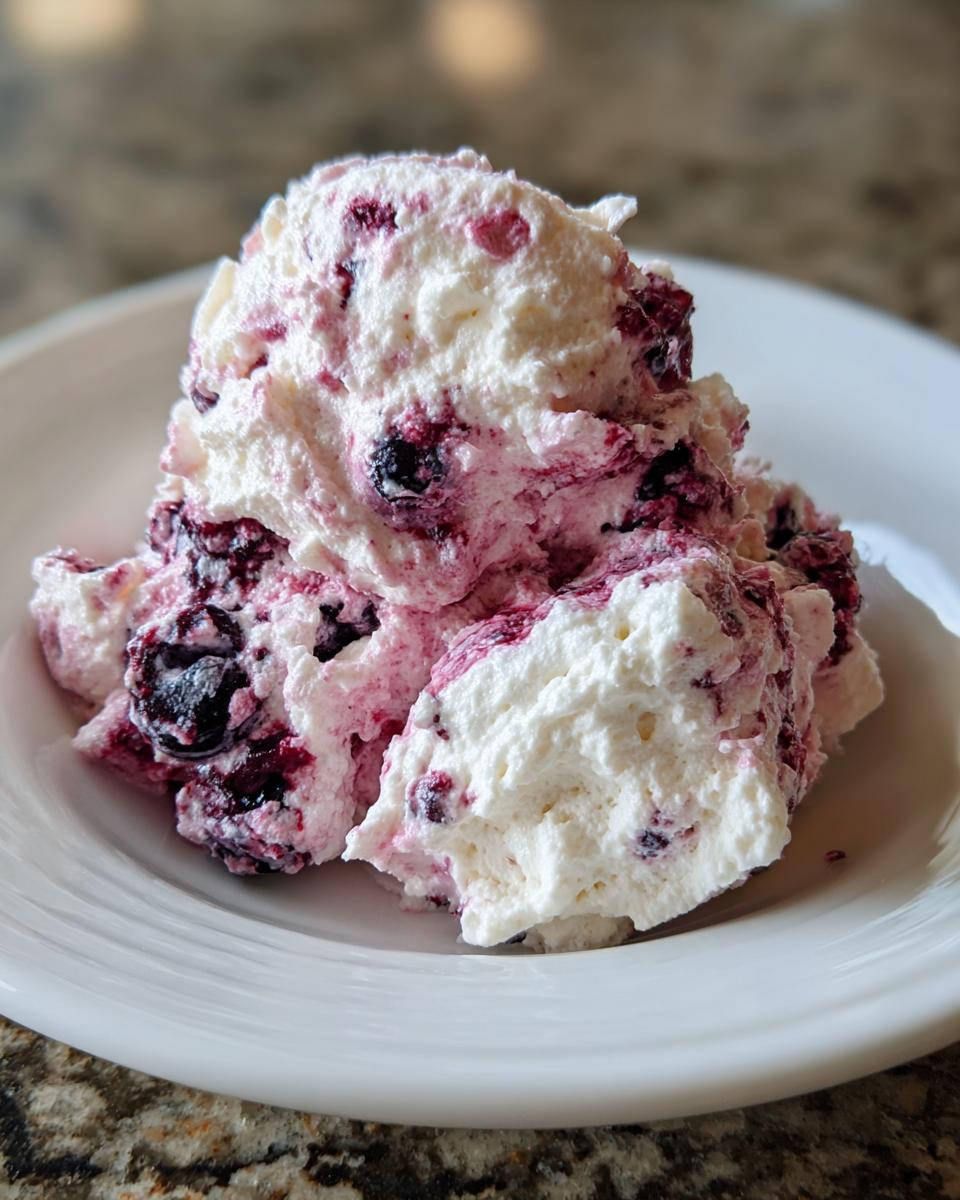 A scoop of creamy, white and pink blueberry fluff salad mixed with whole blueberries, served on a white plate.
